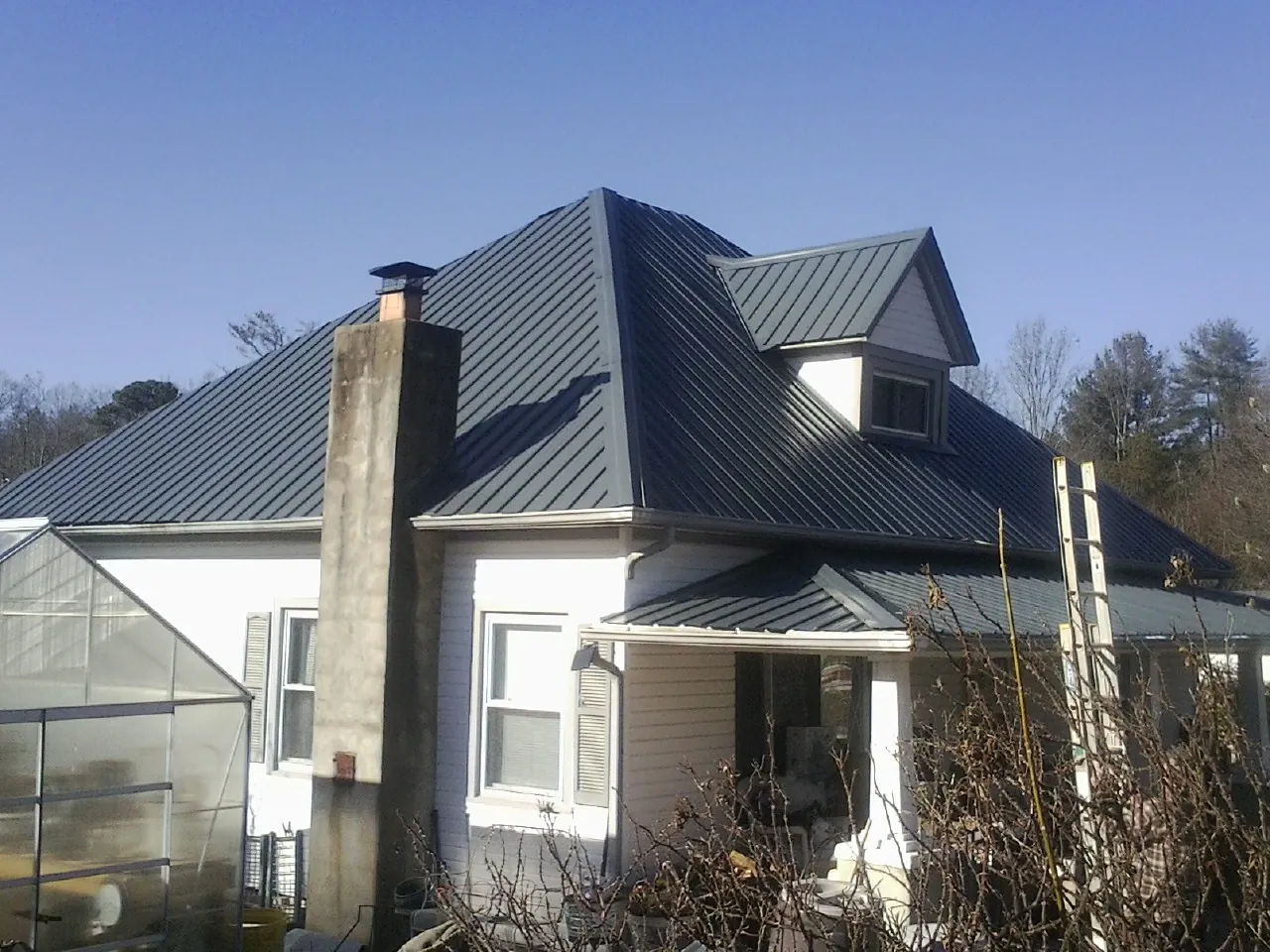 Dark blue standing seam metal roof on a white farmhouse with dormer — Slate & Tile Roof Repair by Roofing Brothers in Lake Geneva