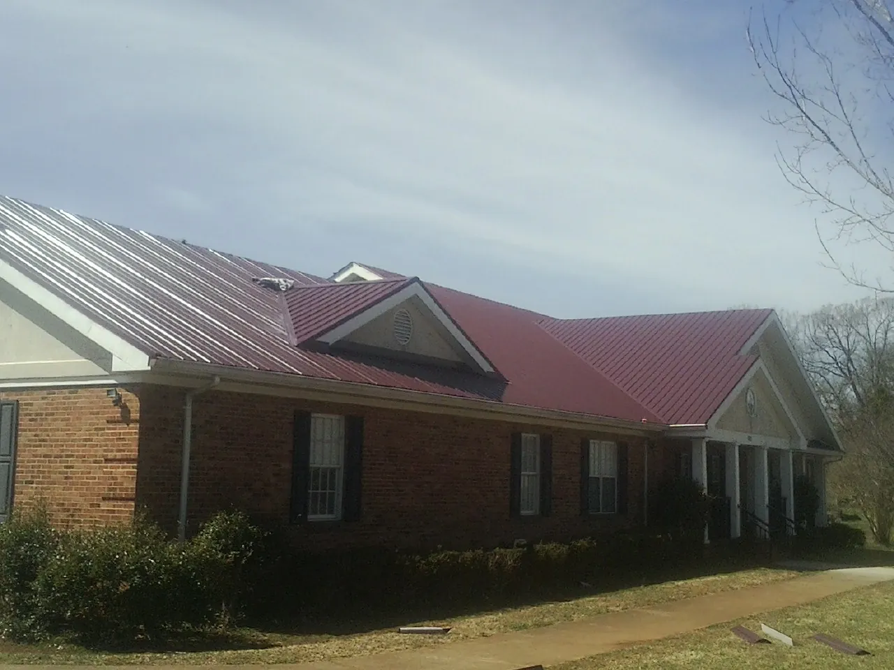 Red metal roof with gabled entries on a long brick building, from a Hail Damage Roof Repair job in Lake Geneva