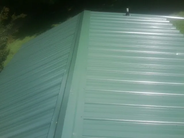 New green metal panels meeting at the ridge of a roof — Flat Roof Repair work by our crew in Lake Geneva