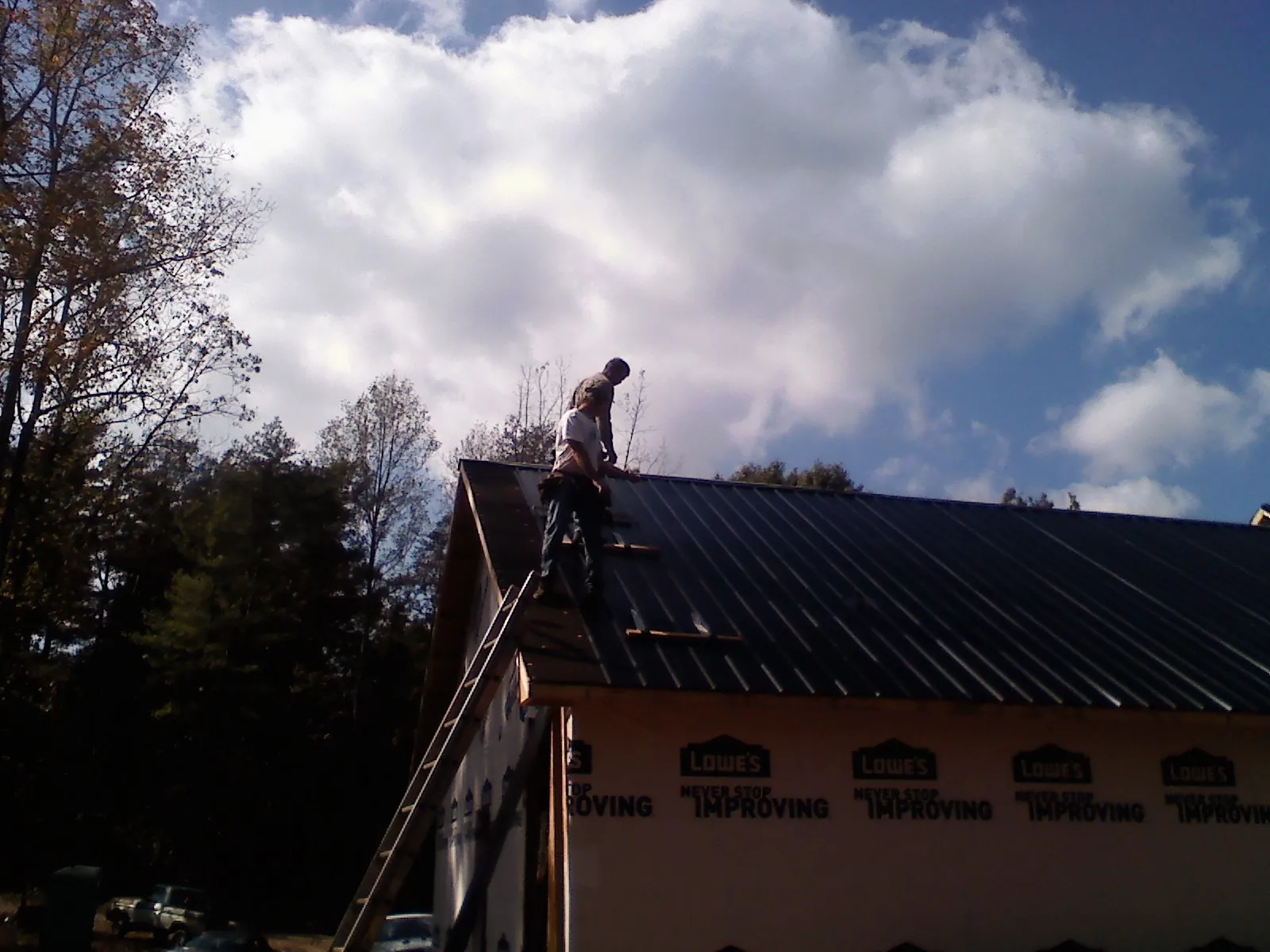 Roofer fastening dark metal panels high against a cloudy sky, from a Roof Inspection job in Lake Geneva