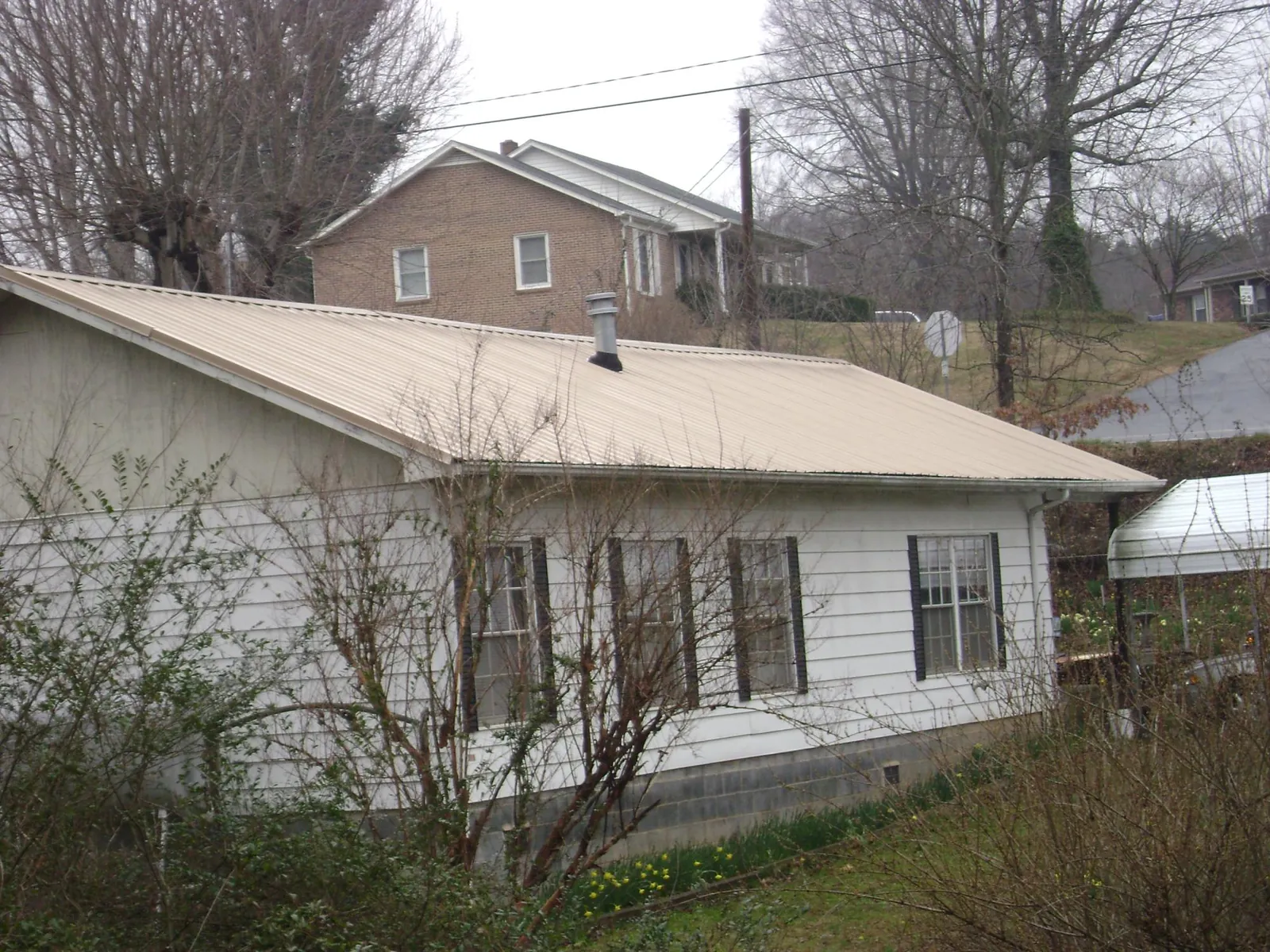 Tan metal roof on a white sided house set into a hillside — Commercial Roofing by Roofing Brothers in Lake Geneva